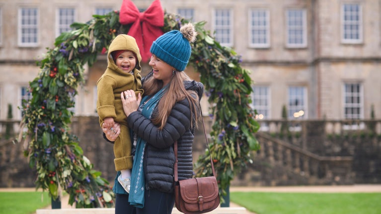 A woman and a young child standing in front of a giant wreath with a historic house behind it